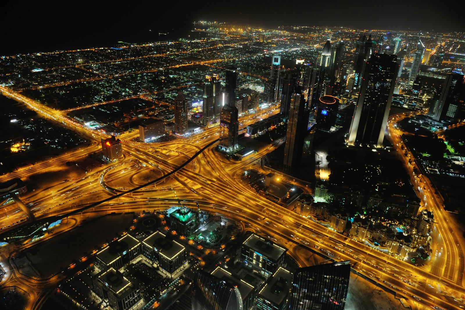 Aerial night view of Dubai showing illuminated highways, urban towers and intersecting transport corridors.