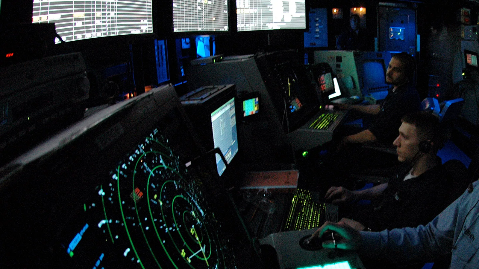 A dark aviation control room with radar displays and operators monitoring traffic.