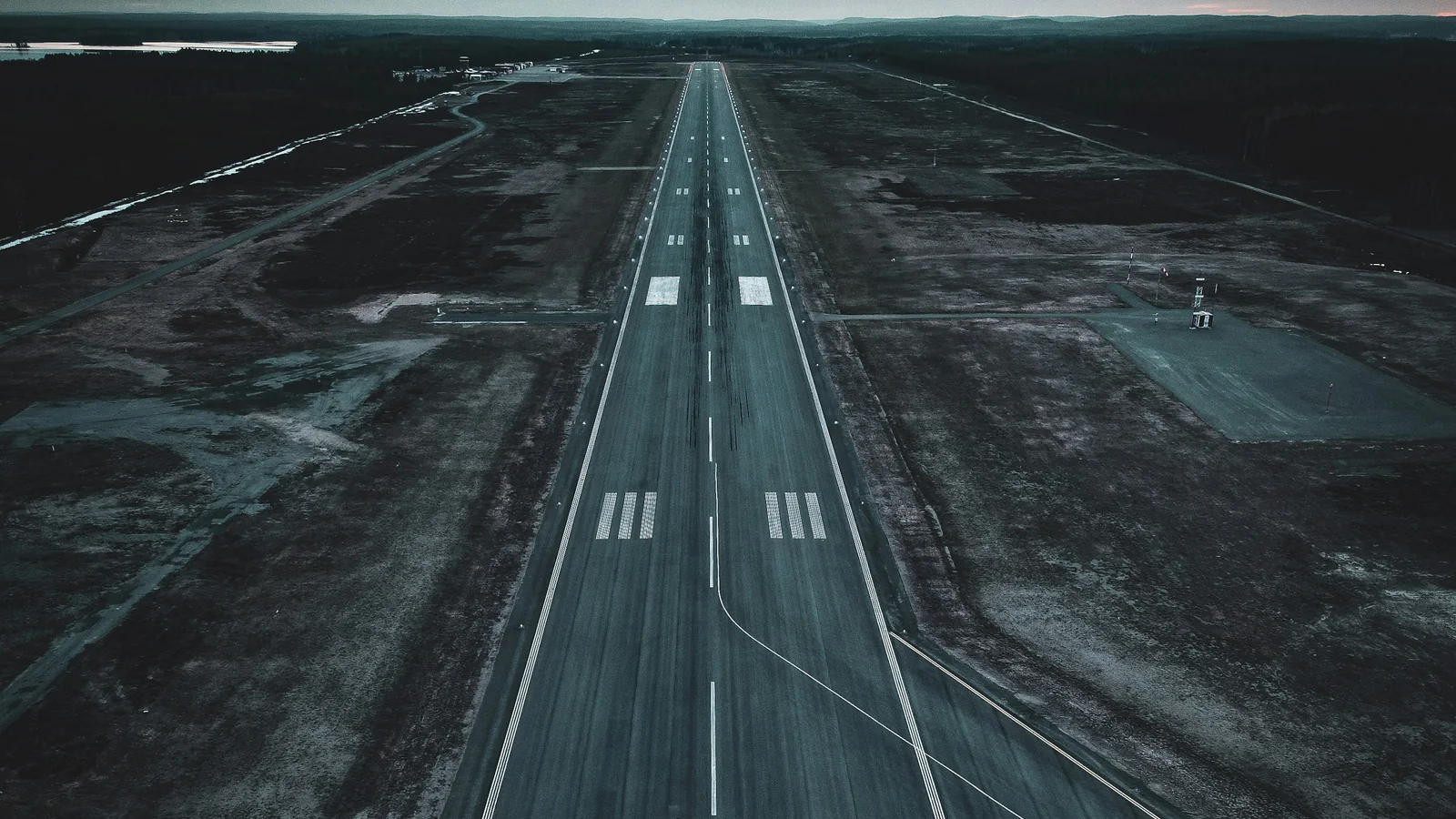 An aerial view of an empty airport runway extending through a dark landscape.
